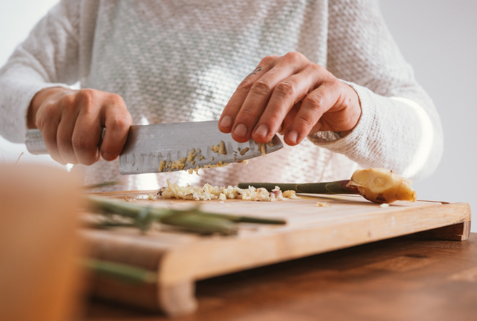 persons hand chopping garlic on cutting board with chefs knife
