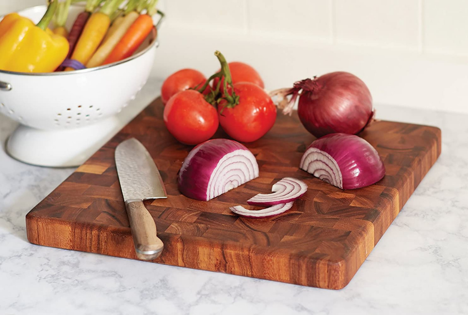 knife with red onions and tomatoes on end grain cutting board