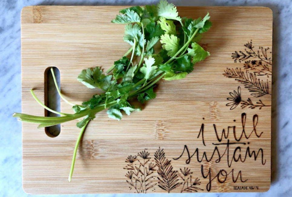 cutting board with wood burnt saying and herbs
