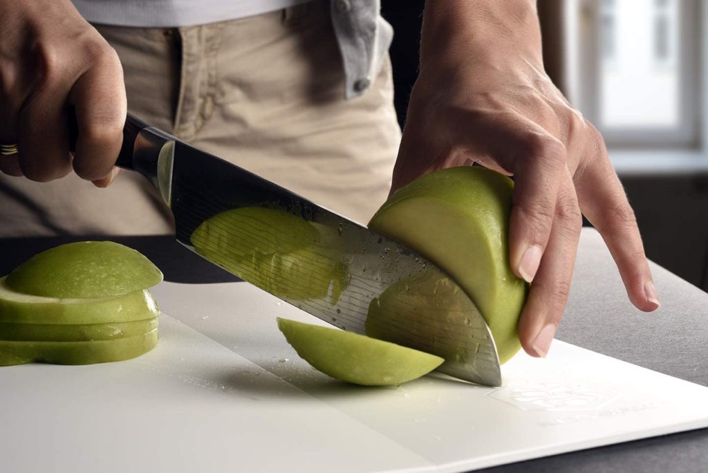 person chopping green apple slices on white cutting board
