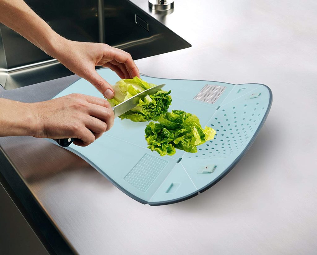 foldable blue cutting board with person holding knife and vegetables on it