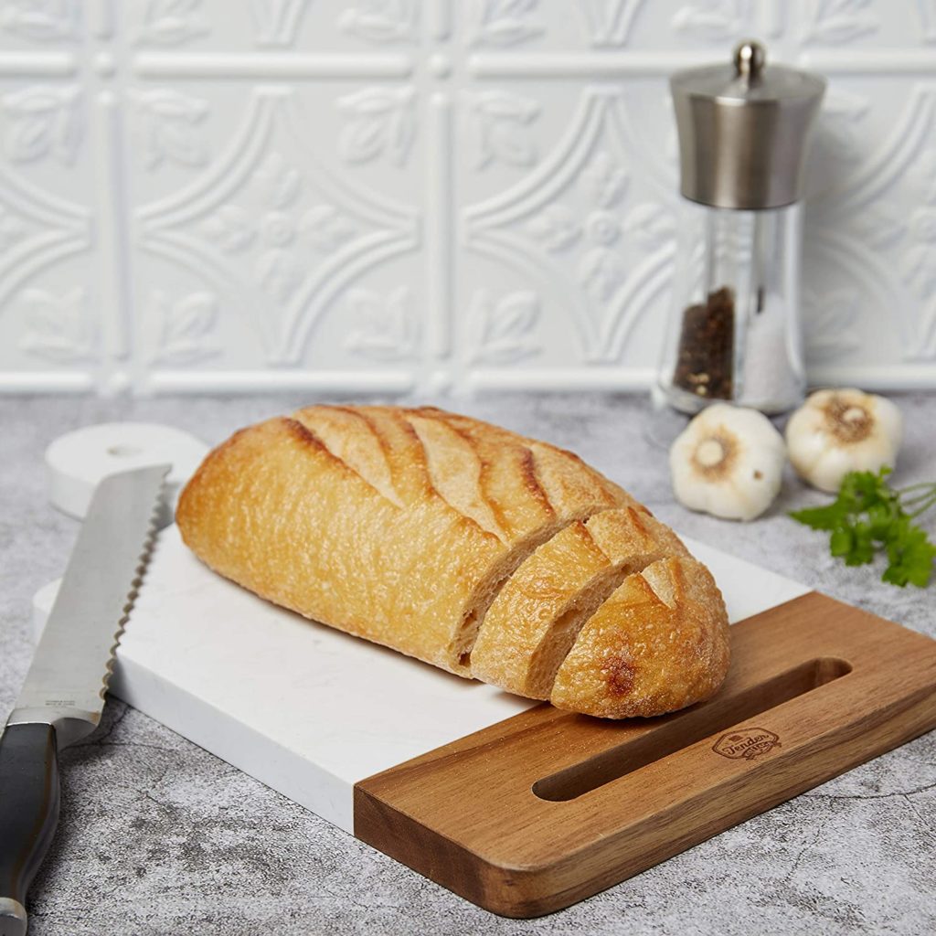 cutting board white in color with wood handle and a loaf of bread on top