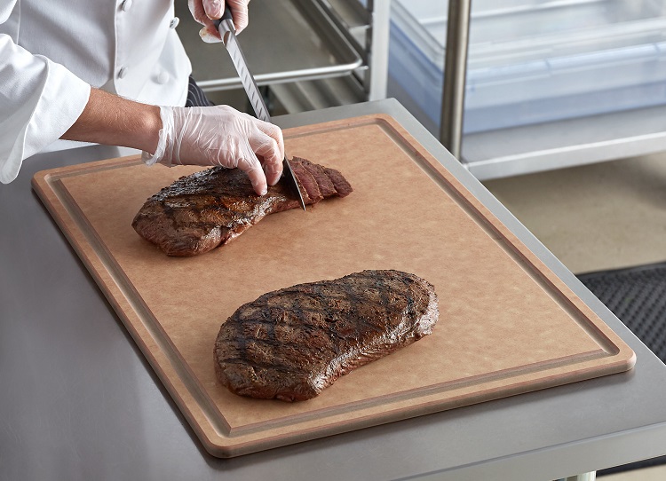 large cutting board with chef cutting two steaks