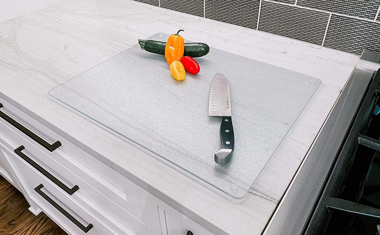 glass cutting board on edge of counter with peppers and knife