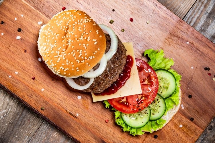 cheeseburger on cutting board with veggies on top