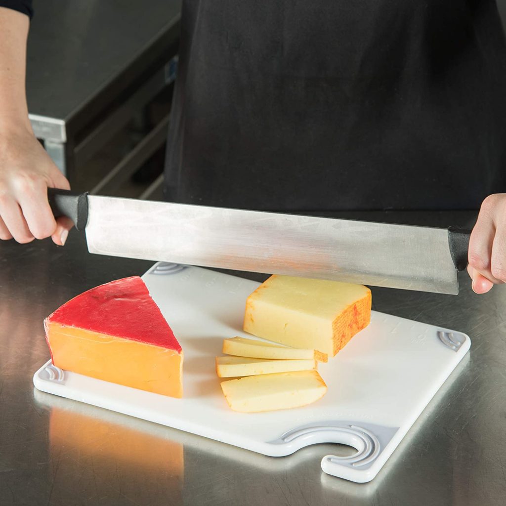 cutting board with person cutting a block of cheese with large knife