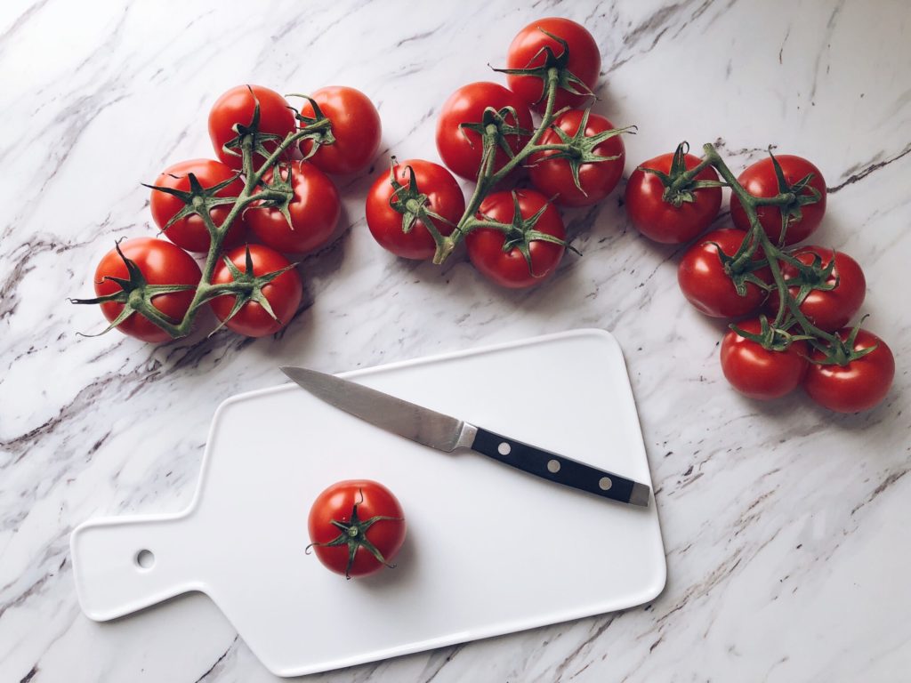 white cutting board with red tomatoes surrounding it