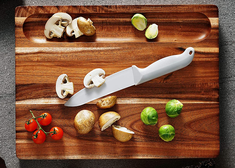 acacia wood cutting board with knife and vegetables on it