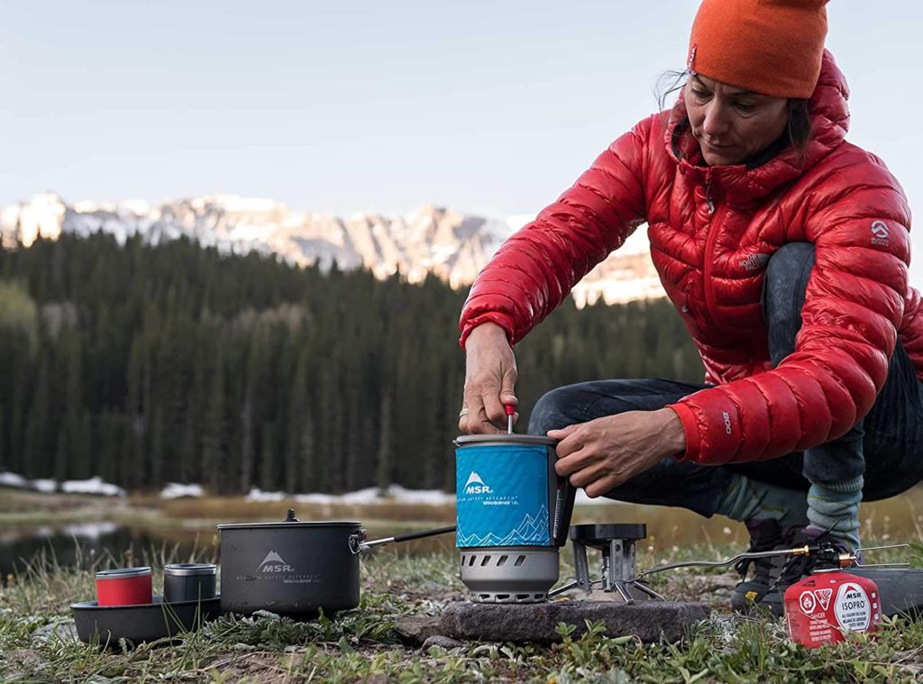 woman camping outside using blue french press coffe machine with other outdoor gear