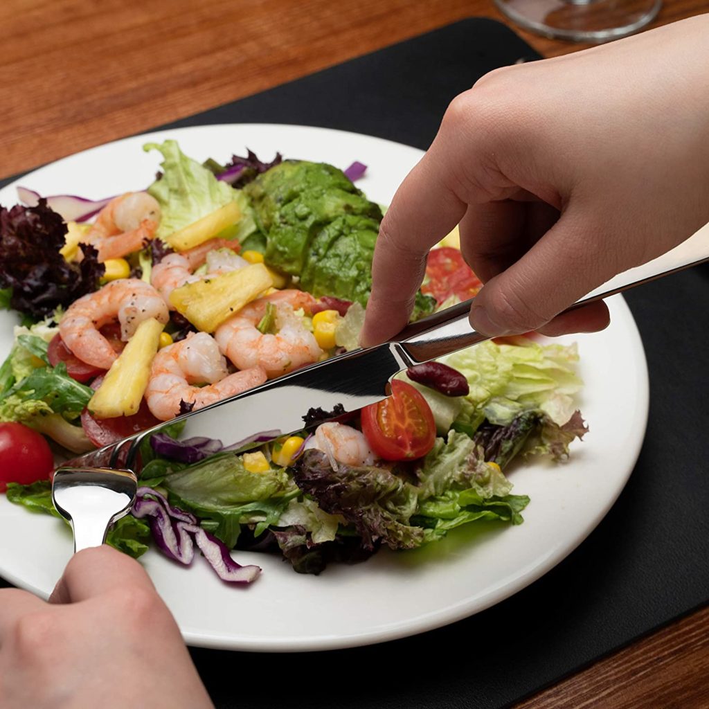 persons hand cutting up shrimp and garden salad with silverware