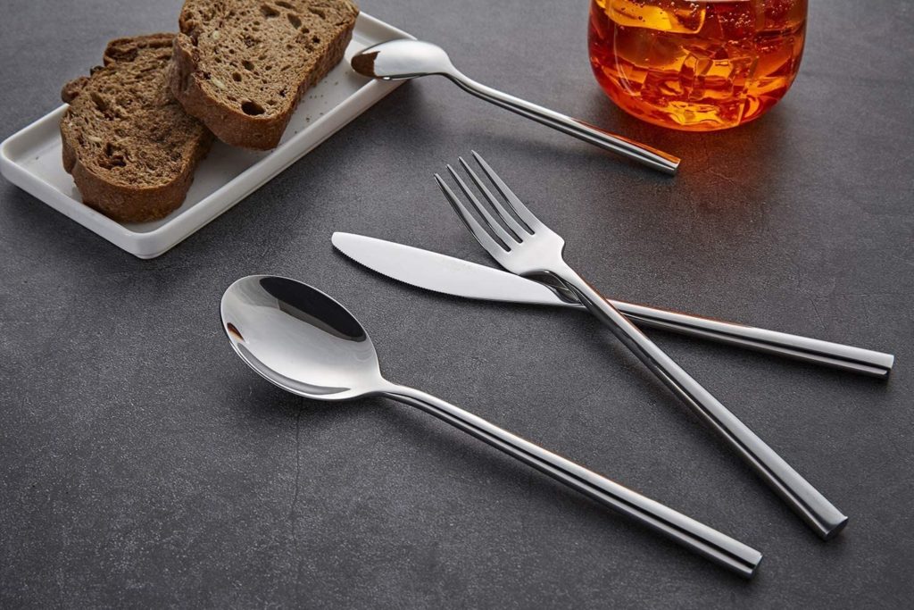 modern stainless steel silverware on stone next to plate of bread