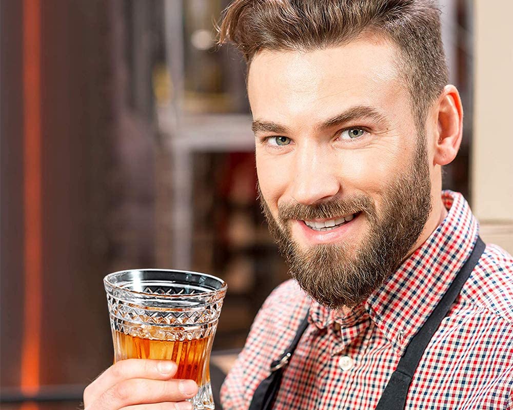 man with beard and plaid shirt holding glass of whiskey