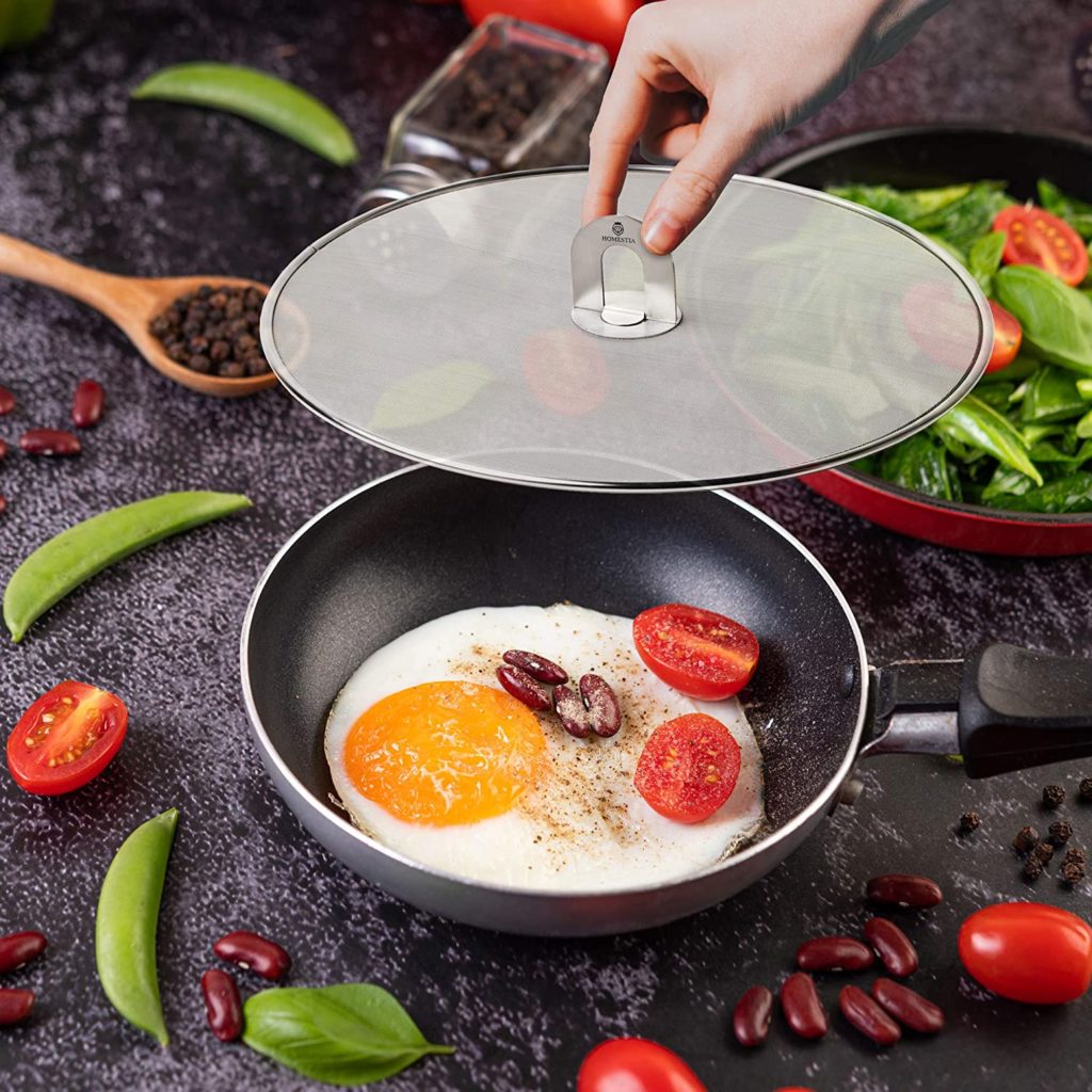 persons hand placing grease splatter screen over pan full of ingredients