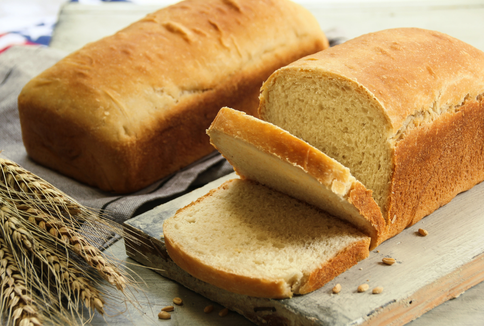 two loaves of partially sliced bread surrounded by wheat