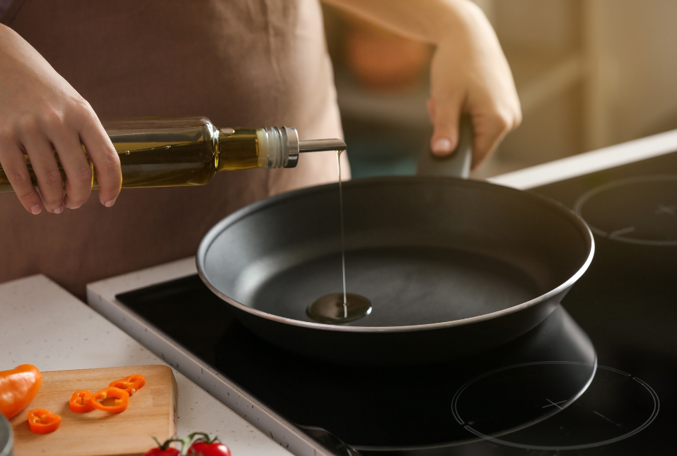 person drizzling olive oil into pan on stove