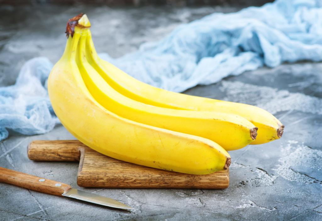 bananas on small wooden cutting board with knife