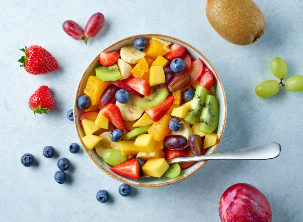 bowl of colorful fresh fruit salad on kitchen table, top view