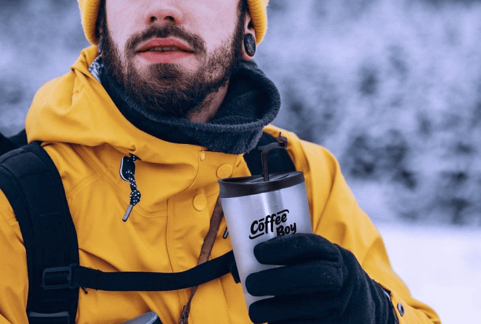 man outdoors in warm gear holding travel coffee mug