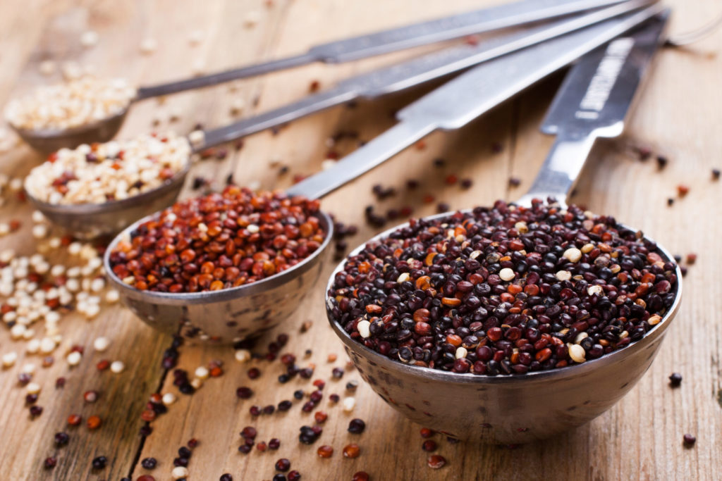 White, red, black and mixed raw quinoa, South American grain, in metal measuring spoons on old wooden background. Healthy food concept. Selective focus.