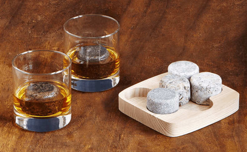 natural whiskey stones in wooden tray next to two glasses of whiskey