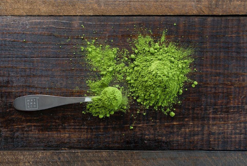 overflowed measuring spoon of matcha green tea powder on wooden table