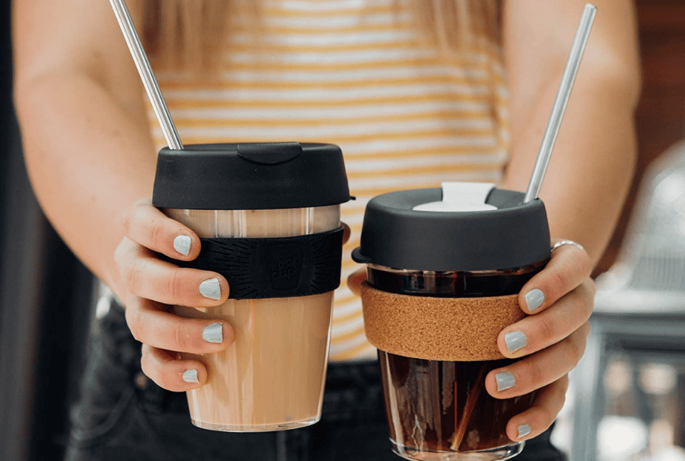 persons outstretched hands holding two insulated travel mugs of coffee