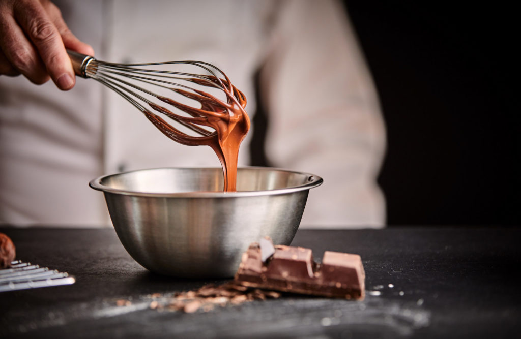 chocolate batter dripping off of whisk into stainless steel mixing bowl