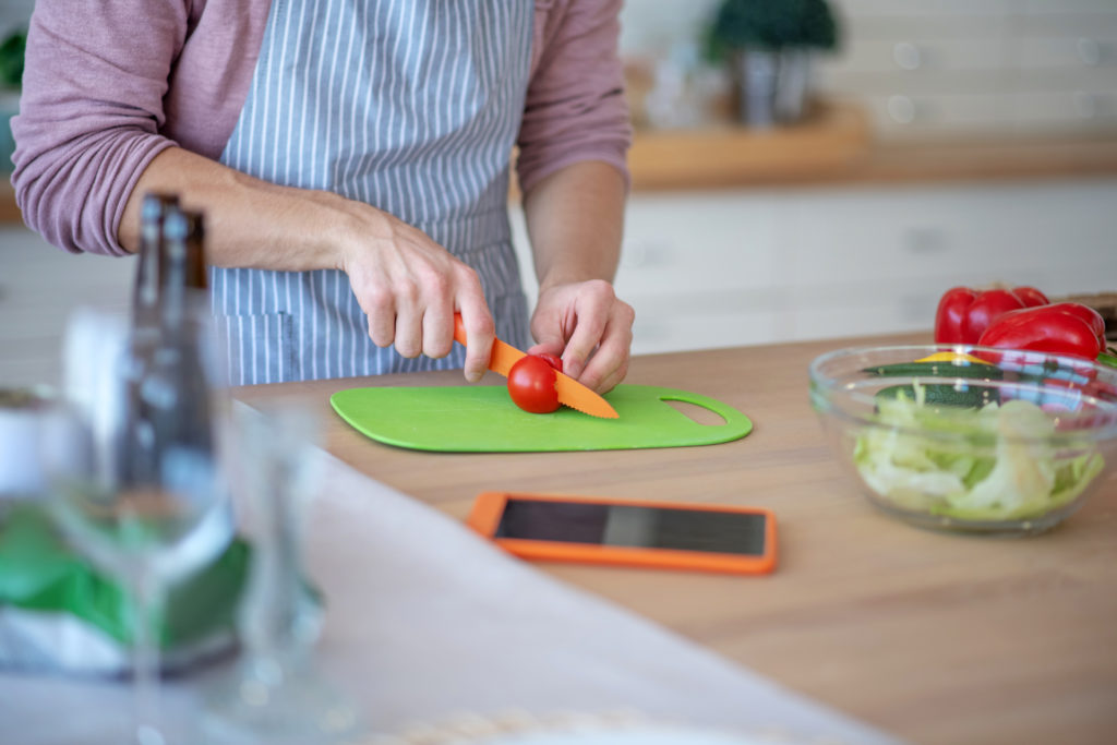 hands cutting tomato on a green cutting board
