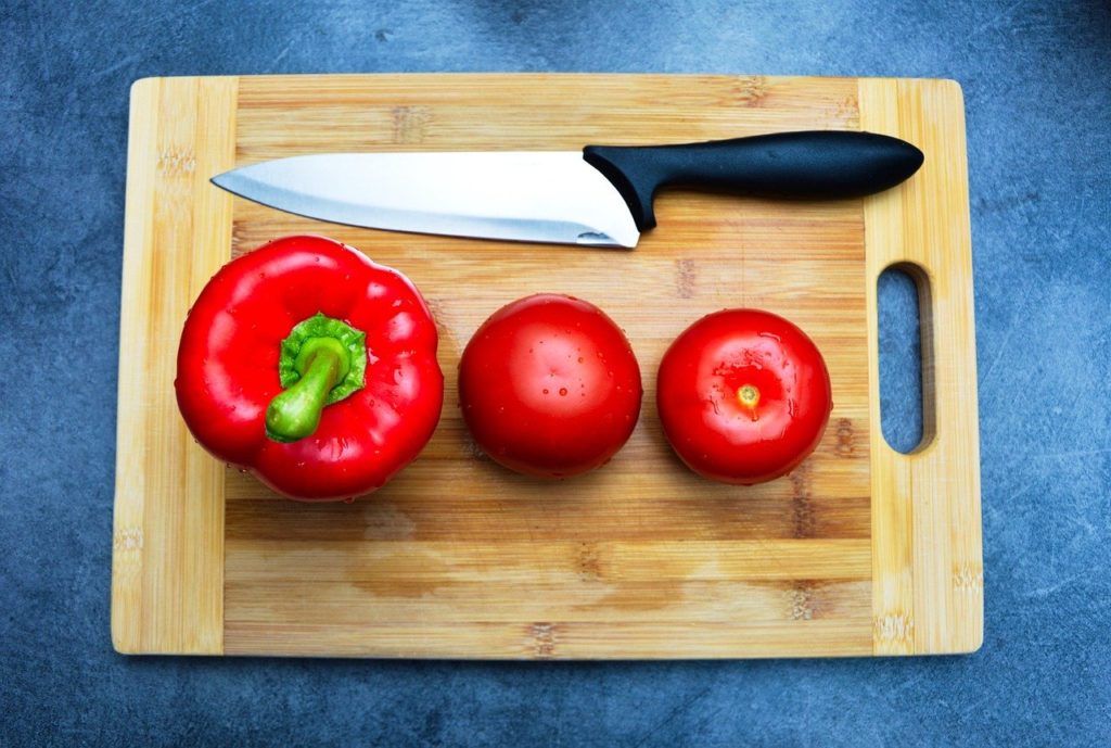 knife and red peppers on bamboo cutting board