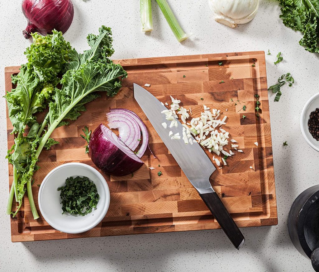onions garlic and produce being chopped on bucher block cutting board