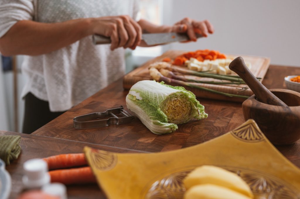 person chopping produce on cutting board with napa cabbage in focus