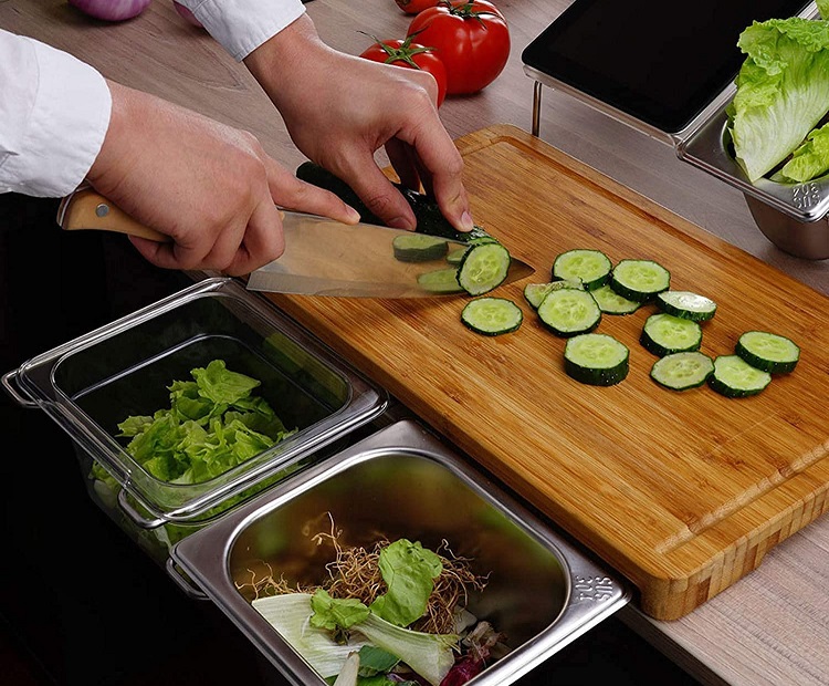 person cutting cucmber on cutting board with stainless steel food prep containers surrounding