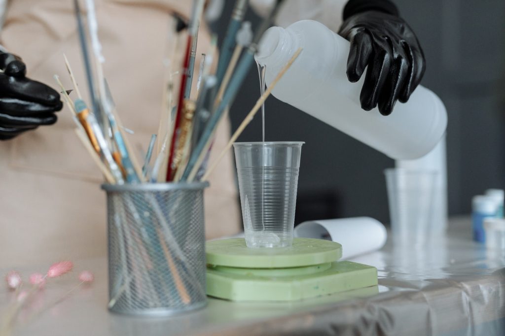 person pouring resin into plastic cup on table with art supplies