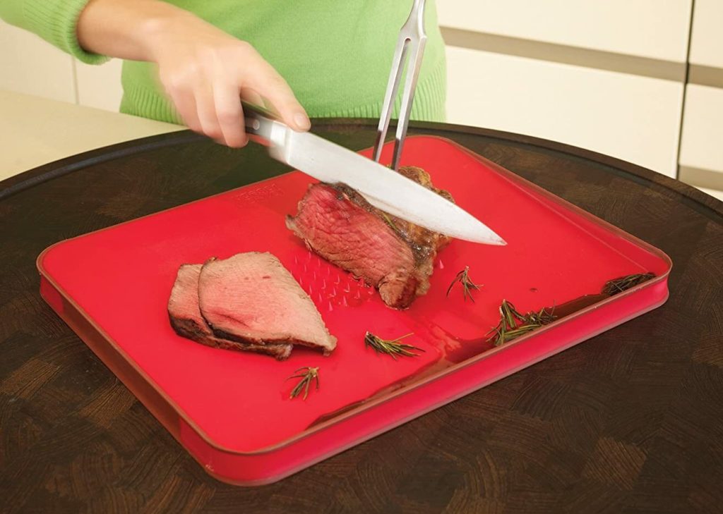 person using chefs knife to slice steak on red cutting board