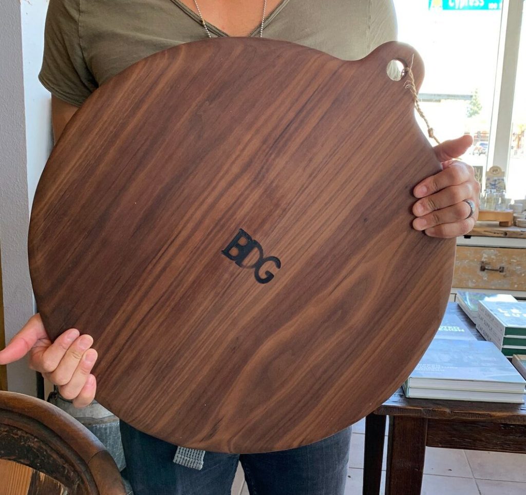 persons hand holding dark wooden round cutting board