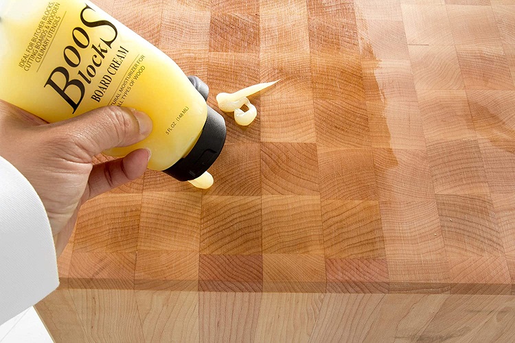 persons hand squeezing boos brand wax on cutting board