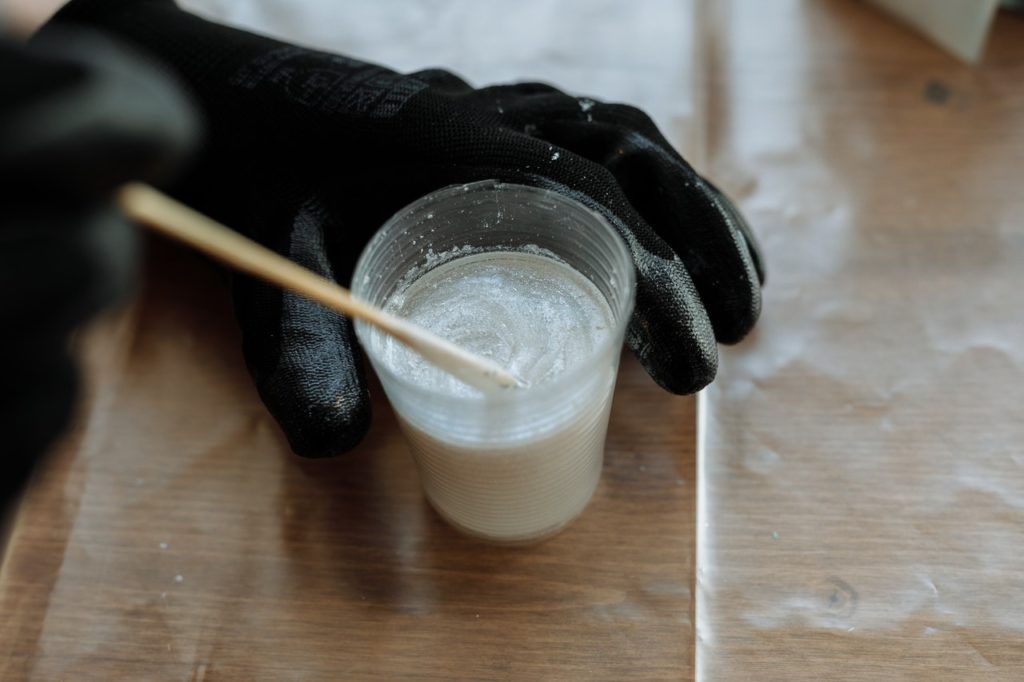persons hand stirring white irridescent resin in plastic cup