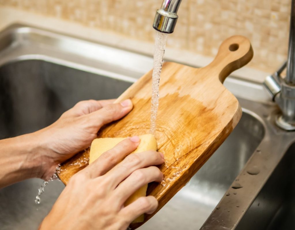 persons hands cleaning wooden cutting baord in sink