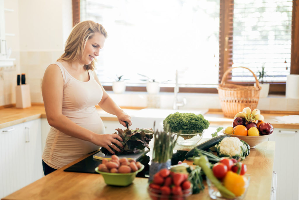 pregnant woman chopping produce in kitchen with butcher block counters