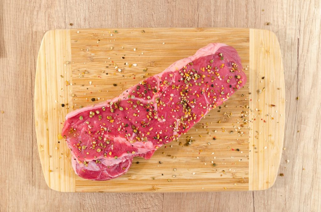 seasoned raw steak on wooden cutting board