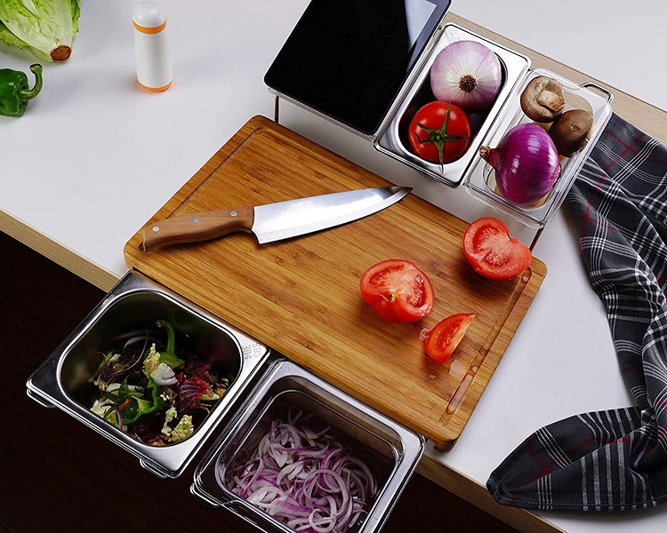 sliced tomato on cutting board surrounded by food prep containers with other produce
