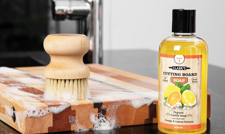 soapy brush cleaning butcher block cutting board with clark brand bottle of cleaner