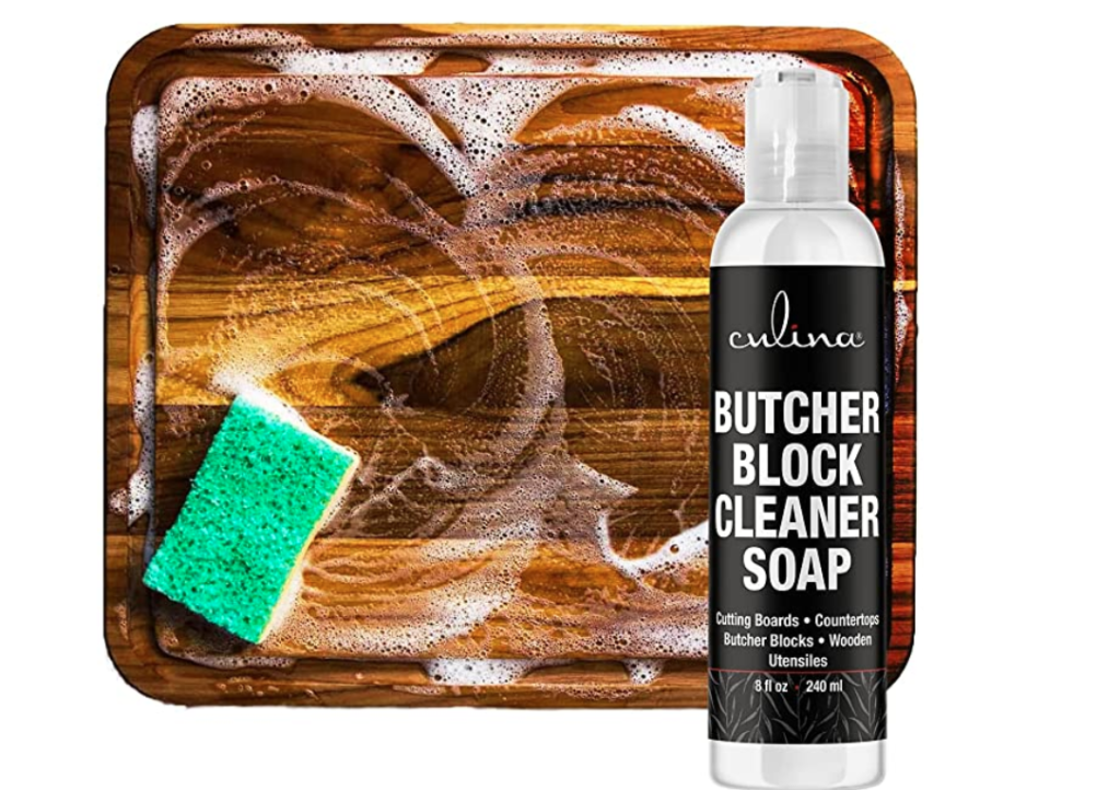 soapy sponge cleaning butcher block cutting board with black and white bottle of cleanser
