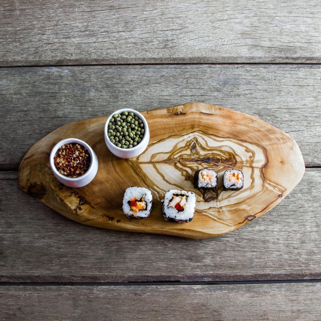 sushi and snacks on irregular oval olive wood cutting board