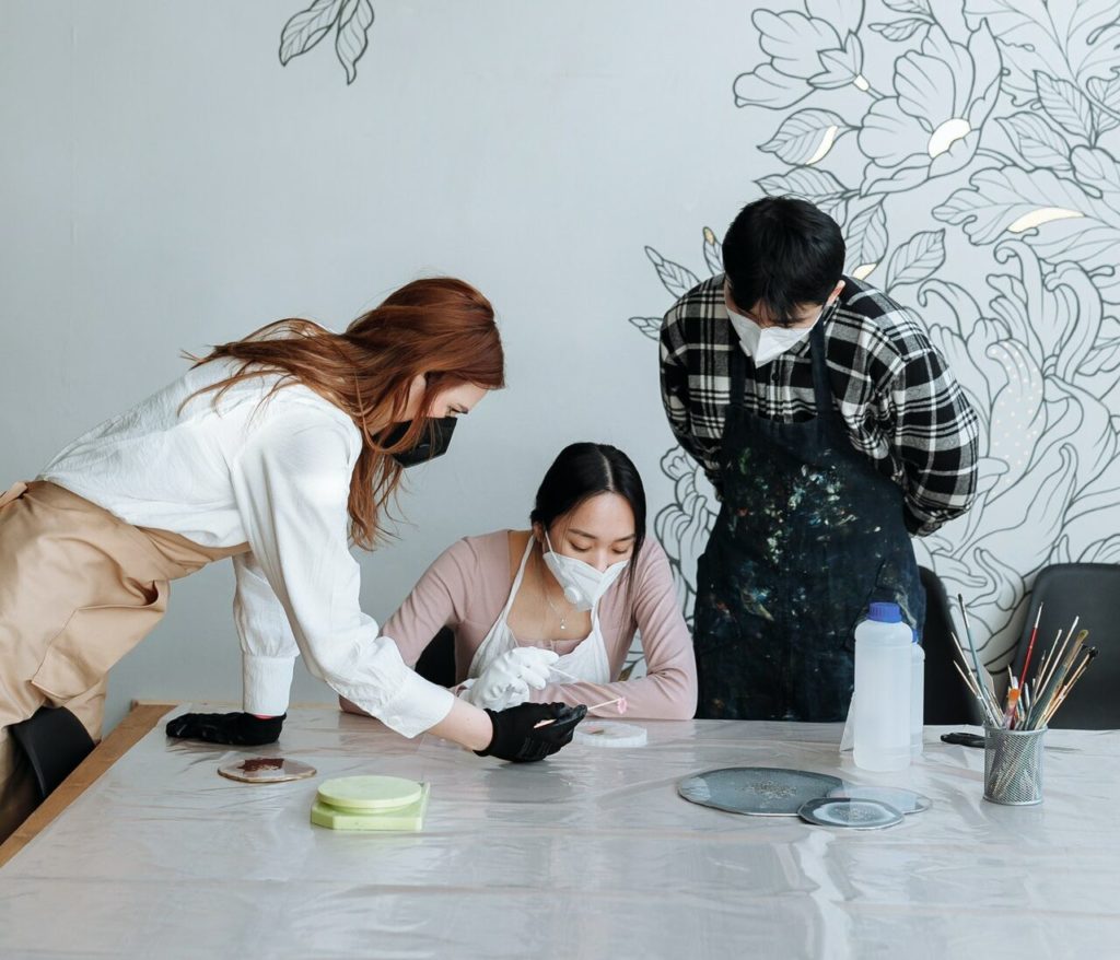 trio of masked people cleaning something on table with acetone and cutips
