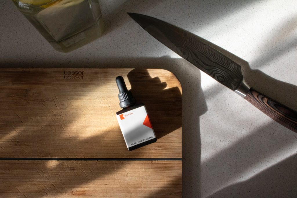 vial dropper of oil over wooden cutting board with knife