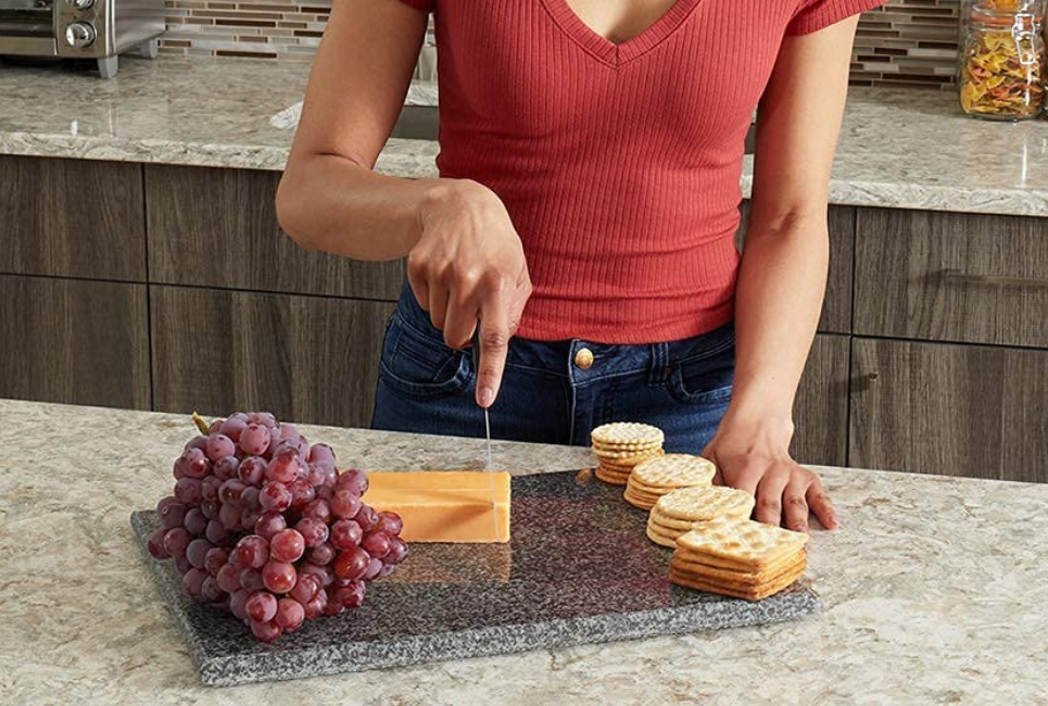 woman cutting cheese on granite snack board