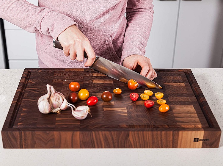womans hand slicing tomatoes and garlic on walnut cutting board
