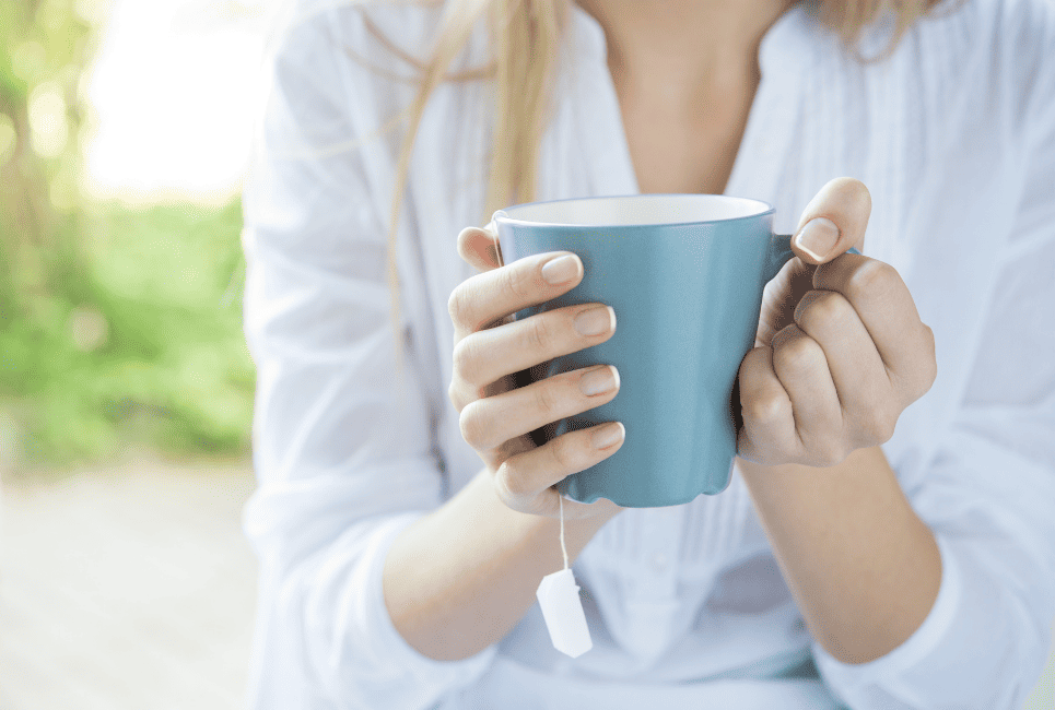 womans hand holding blue ceramic mug with tea bag label dangling out